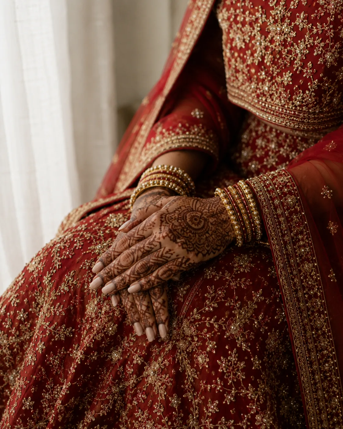 Mehendi hands resting on a crimson lehenga